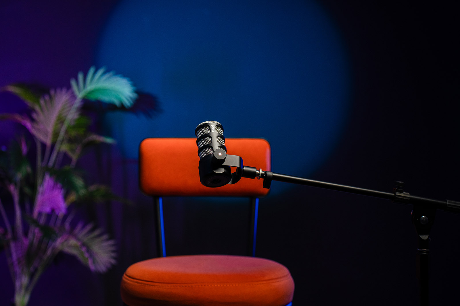 Studio créatif avec chaise orange vibrante, micro professionnel et fond coloré bleu-violet