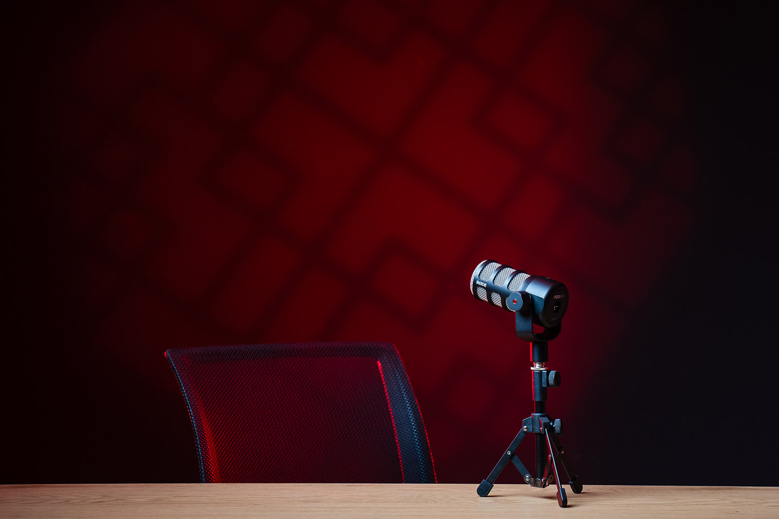 Studio podcast avec éclairage rouge dynamique, micro professionnel et chaise moderne
